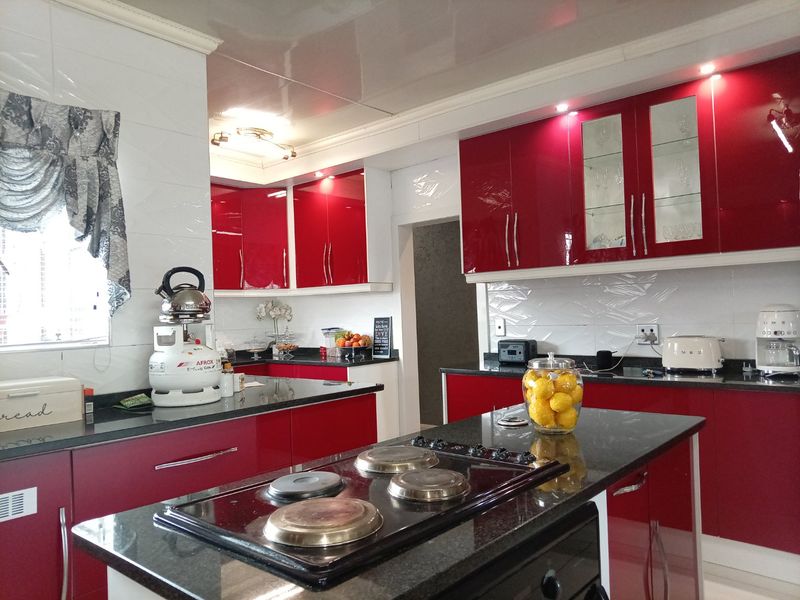 Modern kitchen featuring high-gloss red cabinetry, black granite countertops, a central island with an integrated hob, and tiled backsplash.