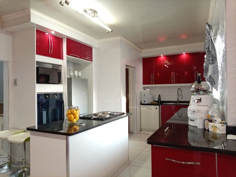 Modern kitchen featuring high-gloss red cabinetry, contrasting black granite countertops, built-in oven, microwave, and gas hob with tiled flooring throughout.