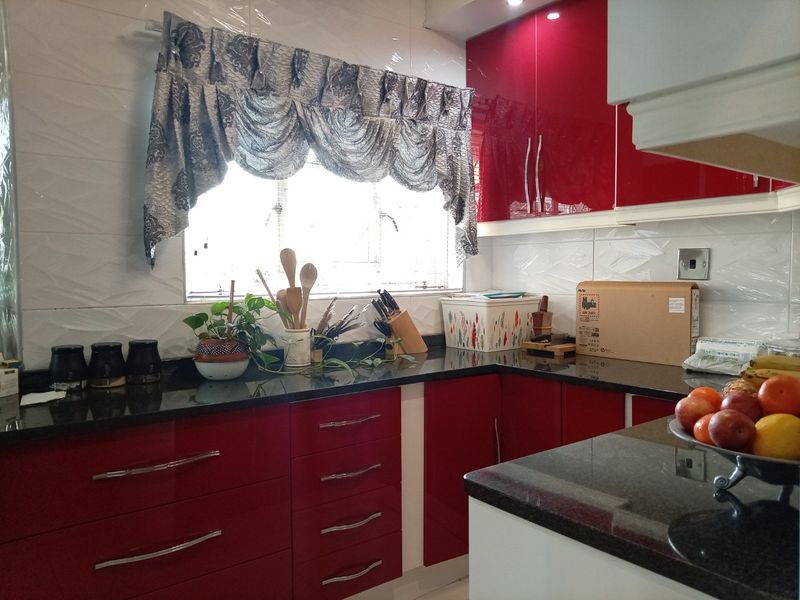 A modern kitchen featuring high-gloss red cabinetry, dark granite countertops, and a tiled backsplash, providing a clean and functional workspace.