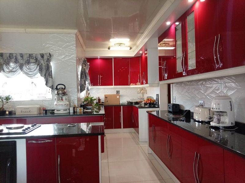 A modern kitchen featuring high-gloss red cabinetry, contrasting black granite countertops, built-in appliances, and tiled flooring with recessed lighting.