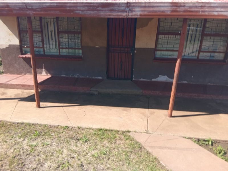 Front exterior view of the house featuring a covered porch, security gate, and security bars on windows, showing signs of significant weathering and paint deterioration.
