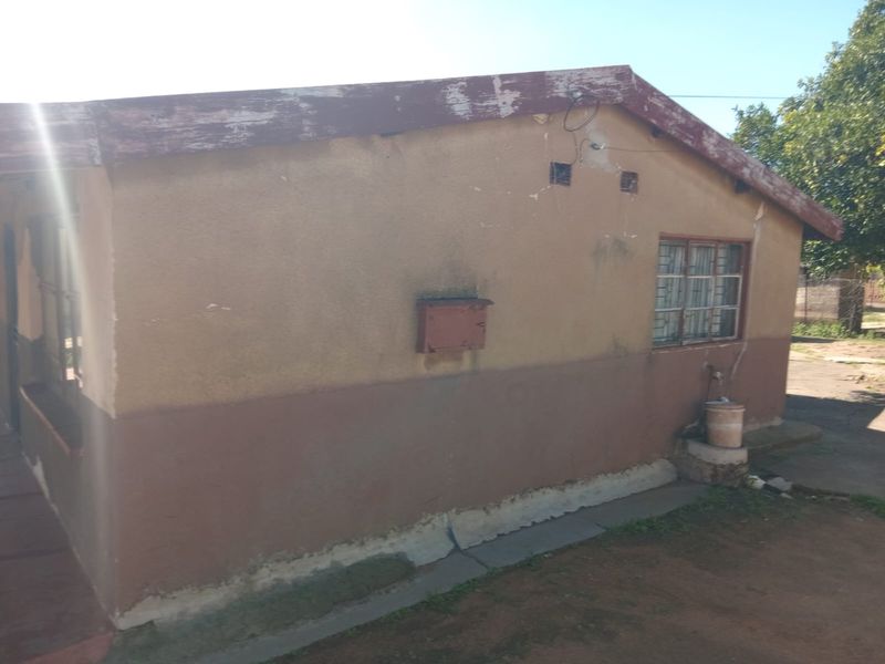 Rear exterior view of the house showing weathered walls, peeling fascia boards, and security bars on the windows.