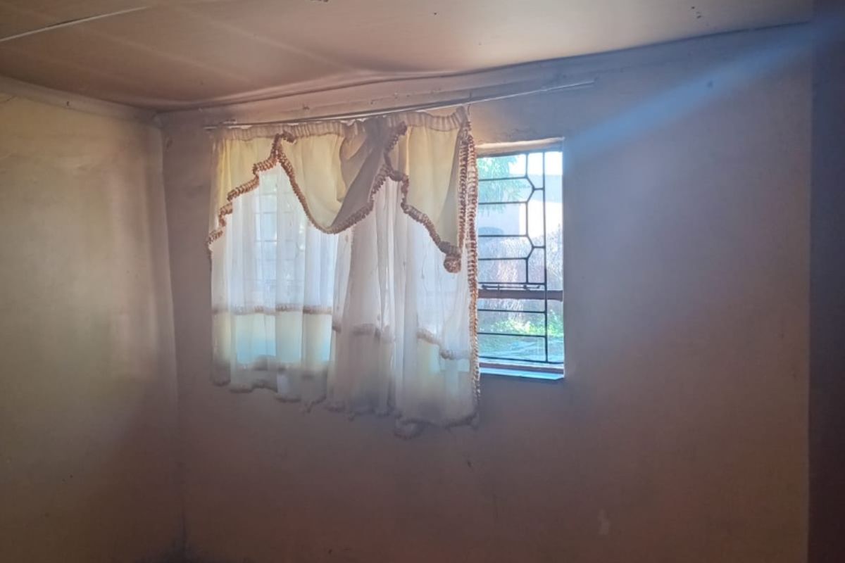An empty bedroom featuring tiled flooring, security bars on the window, and a ceiling in need of repair.
