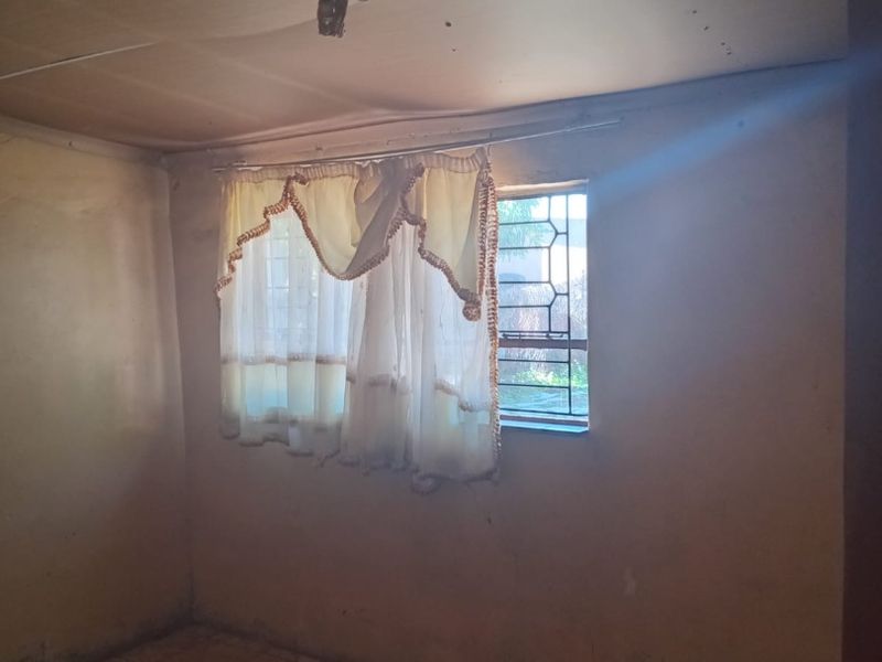 An empty bedroom featuring tiled flooring, security bars on the window, and a ceiling in need of repair.