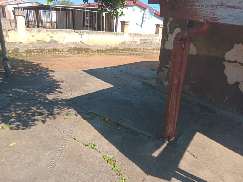 Rear exterior area featuring a cracked concrete patio, a downpipe, and a boundary wall showing signs of significant weathering and paint deterioration.