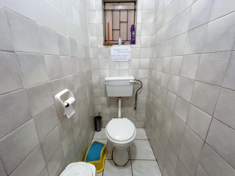 A compact bathroom featuring full-height ceramic wall tiling, a standard toilet with a high-level cistern, and a small window with security bars.