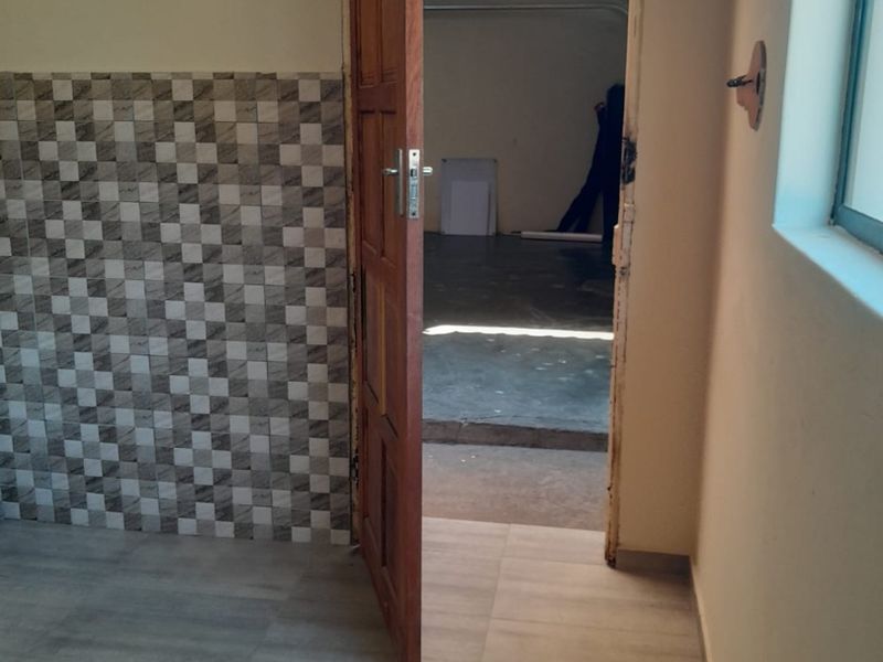 A utility space featuring tiled flooring and a partial tiled wall, leading through a timber door into an adjacent unfinished area.