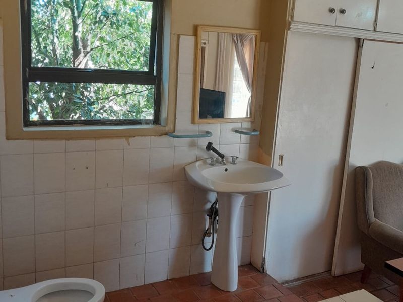 A dated bathroom featuring a pedestal basin, toilet, and tiled flooring, requiring cosmetic updates to modernize the space.