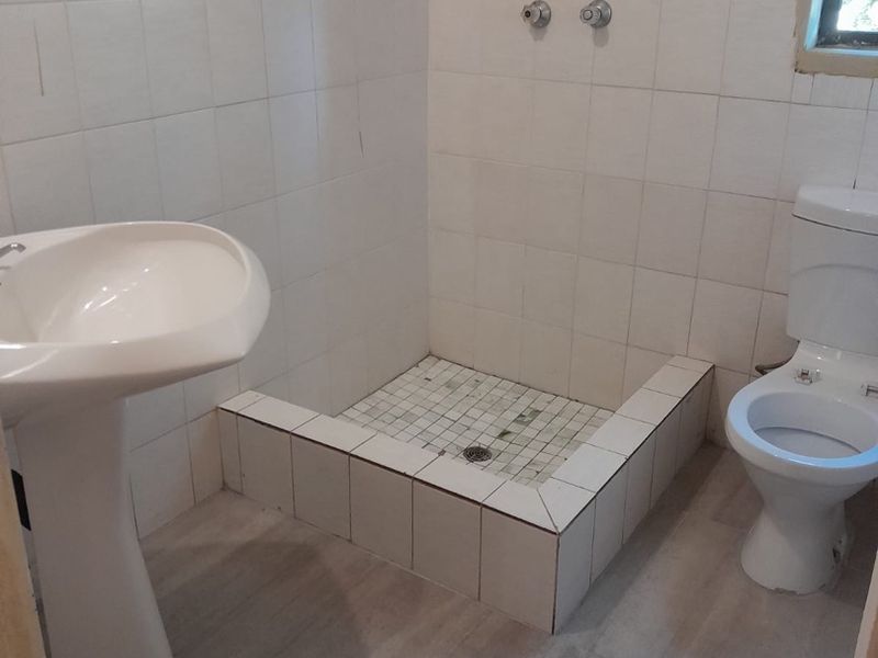 A functional bathroom featuring a pedestal basin, toilet, and a tiled shower base. The space requires new shower fixtures and finishing touches.