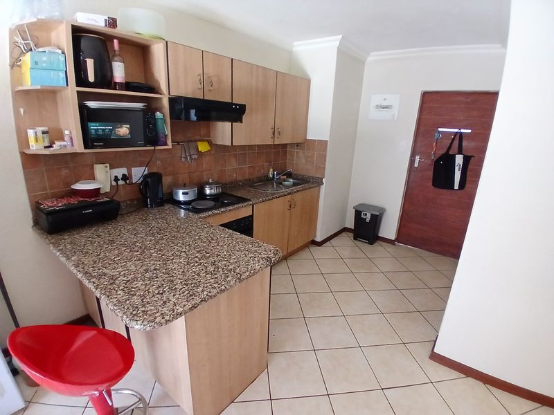 Compact kitchen featuring granite countertops, laminate cabinetry, built-in hob with extractor fan, and tiled flooring.