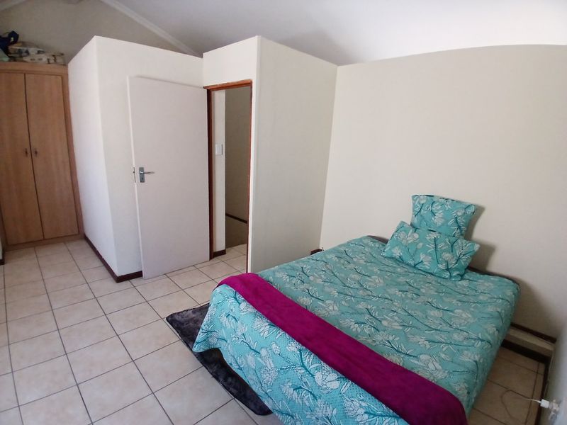 A bedroom featuring tiled flooring, a vaulted ceiling, and a built-in wardrobe, providing a functional and neutral living space.