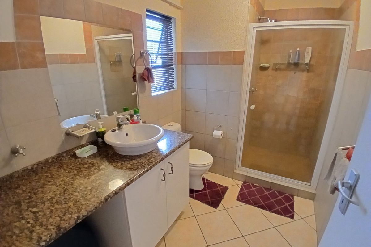 A functional bathroom featuring a granite-topped vanity, a separate shower enclosure, and neutral wall and floor tiling.