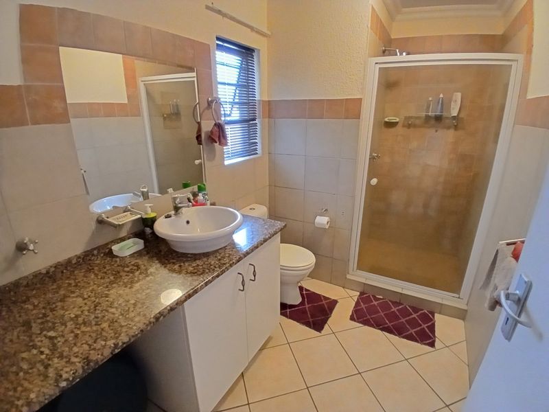 A functional bathroom featuring a granite-topped vanity, a separate shower enclosure, and neutral wall and floor tiling.