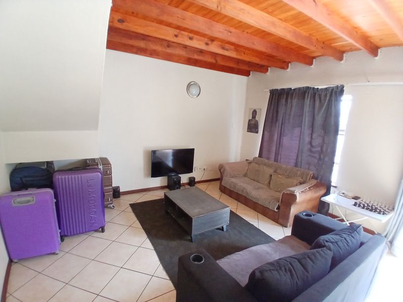 Living room featuring exposed timber ceiling beams and ceramic floor tiles, with an adjacent staircase.