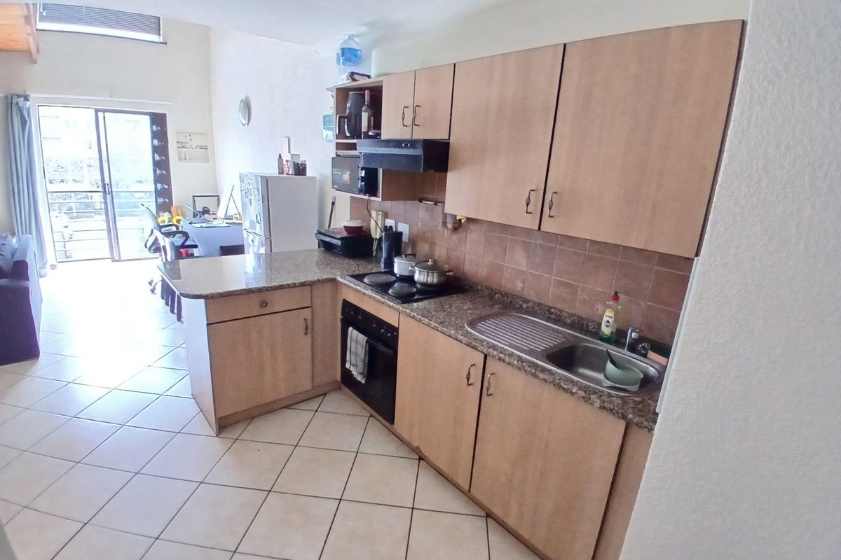 Open-plan kitchen featuring laminate cabinetry, granite countertops, and built-in appliances, flowing into a living area with access to a balcony.