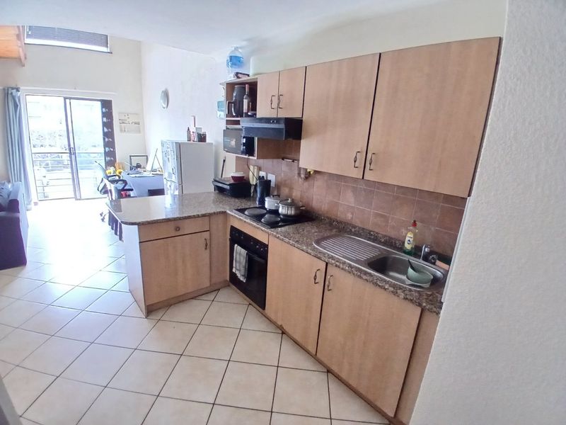 Open-plan kitchen featuring laminate cabinetry, granite countertops, and built-in appliances, flowing into a living area with access to a balcony.