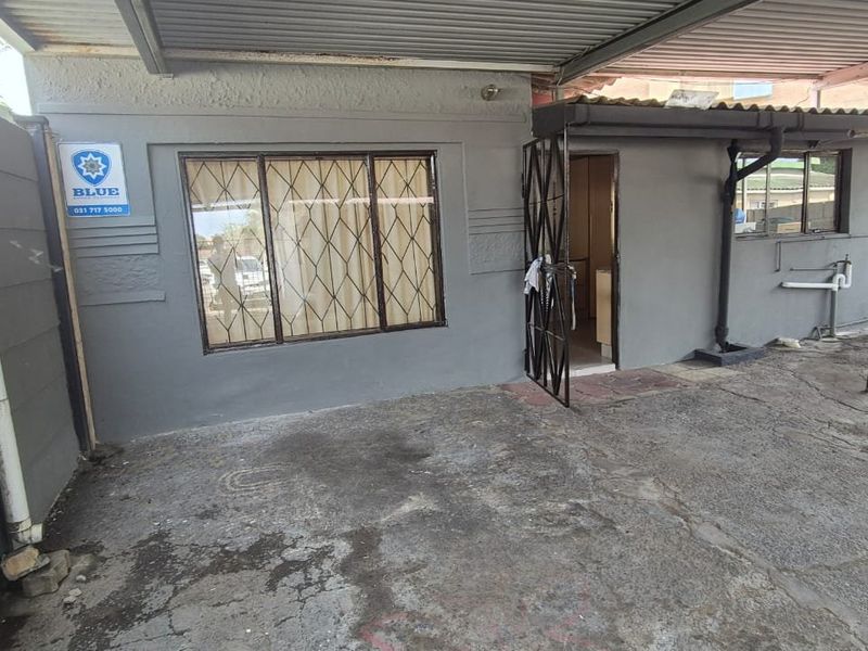 Rear exterior area featuring a covered patio space with concrete paving, security gate, and security bars on the window.