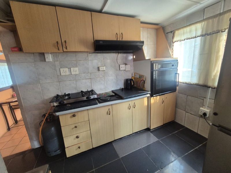 A compact kitchen featuring built-in cabinetry, a gas hob, an extractor fan, and a built-in oven with tiled splashbacks and flooring.