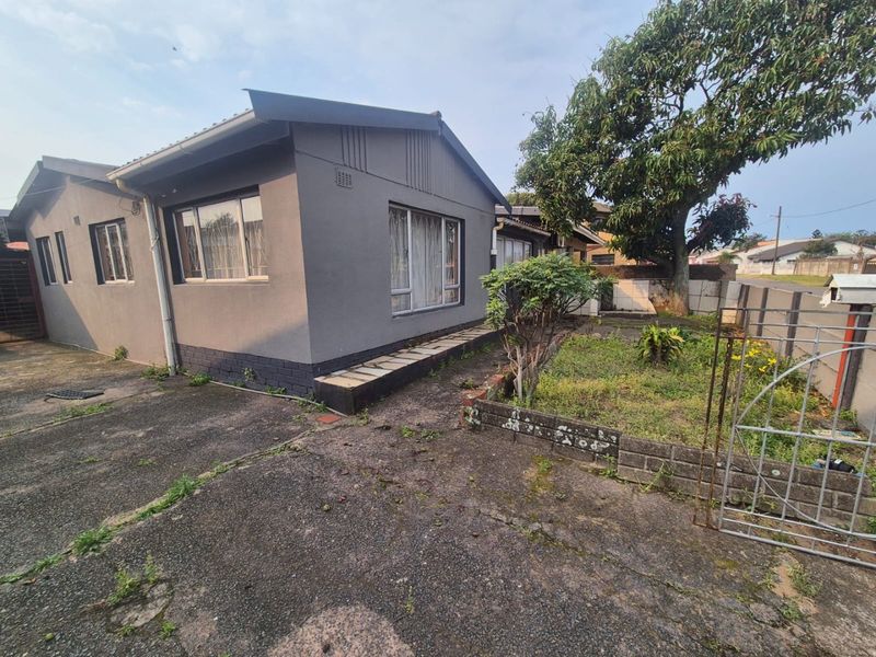 Front exterior view of a detached house featuring a concrete driveway, garden area, and brick boundary wall with metal gate access.