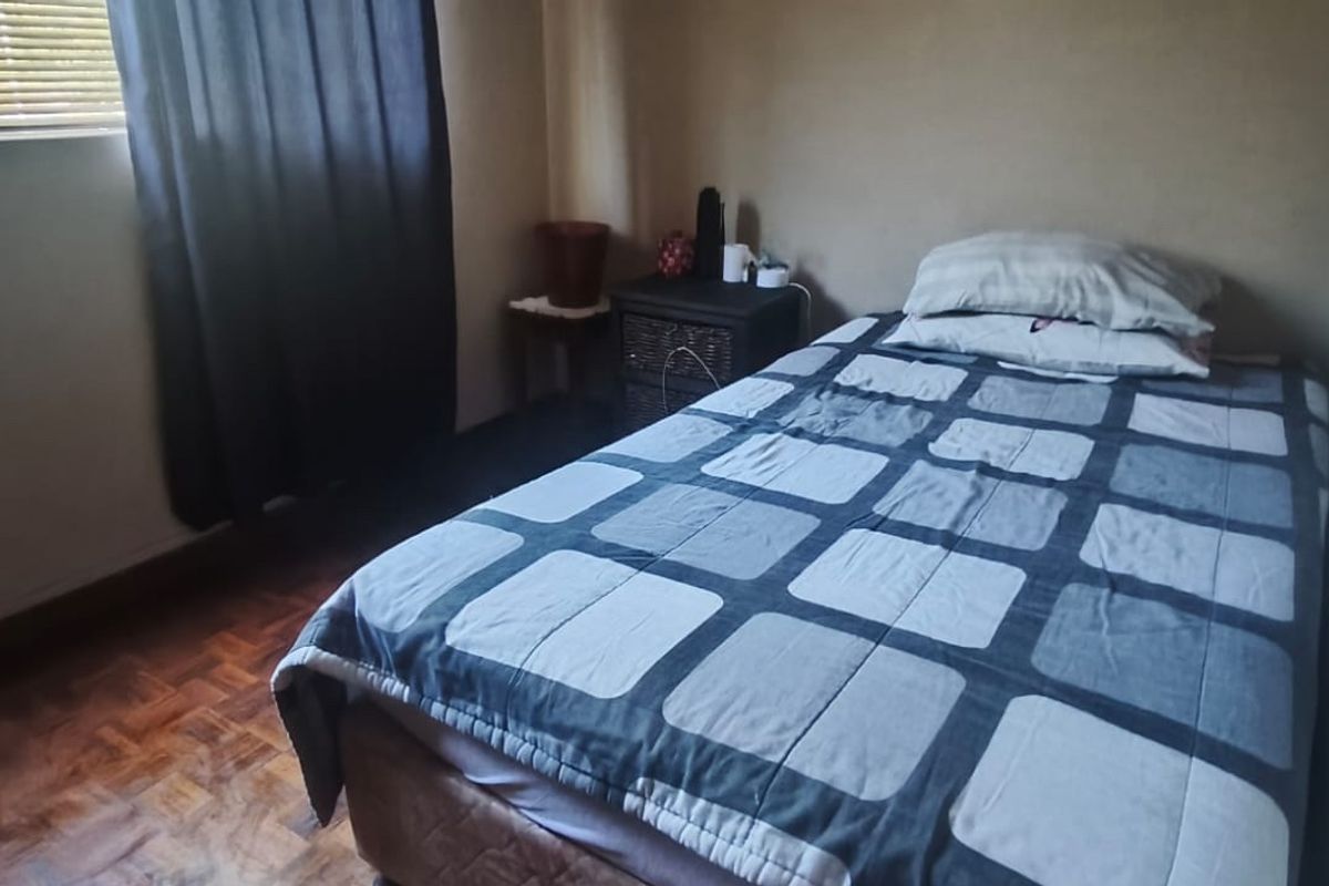 A compact bedroom featuring classic parquet flooring and window blinds, offering a functional space with neutral wall finishes.