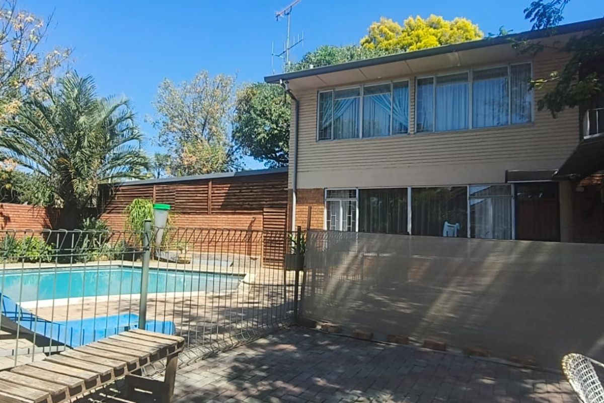 Rear exterior view featuring a swimming pool, paved patio area, and two-story residential building with large windows and sliding door access.