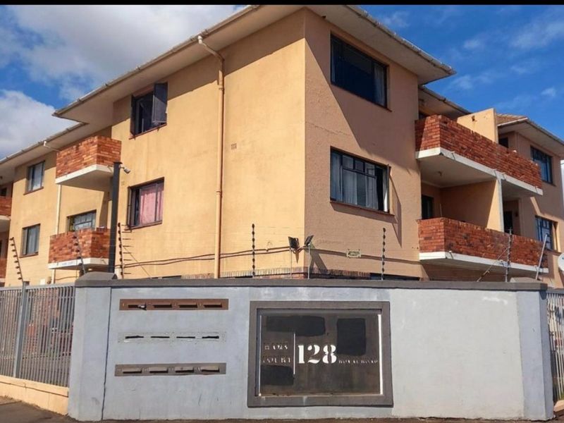 Exterior view of a multi-story apartment building featuring brick balconies, secure perimeter wall with electric fencing, and integrated mailboxes.