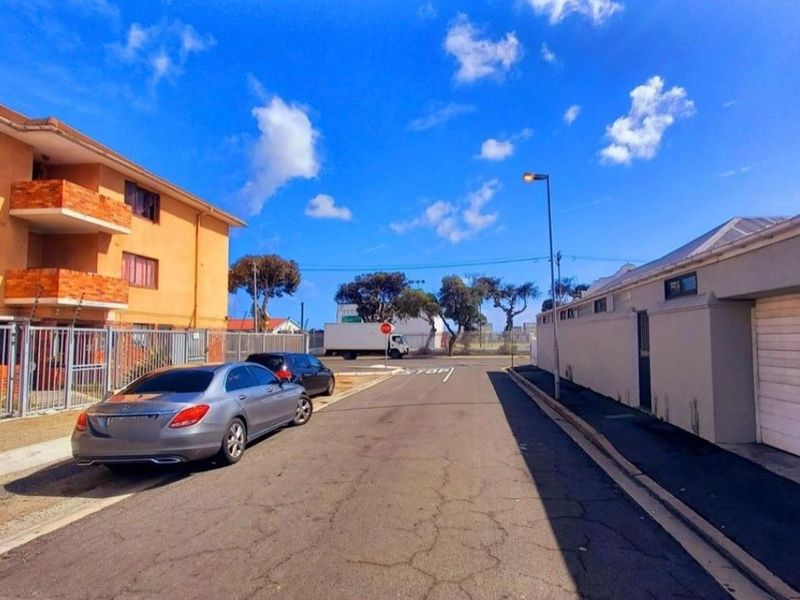 A street-level view showing the exterior of an apartment building with security fencing and adjacent garage structures.