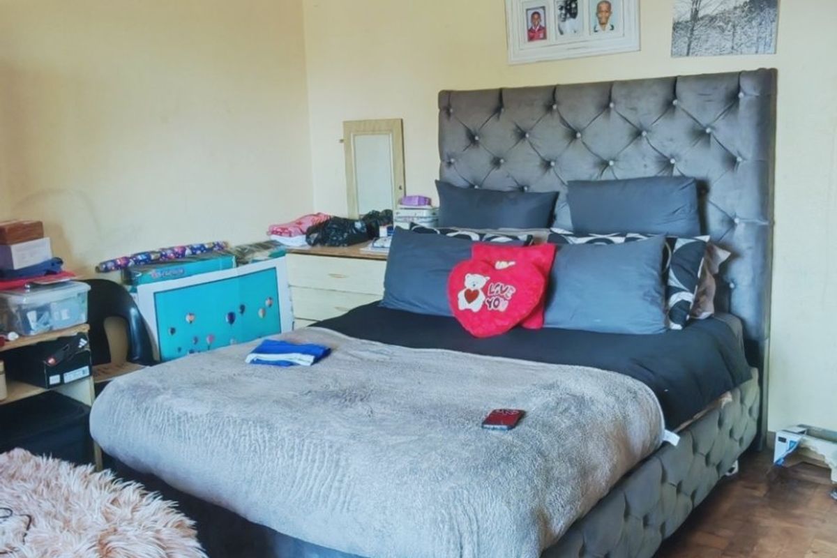 A bedroom featuring parquet flooring and a tiled ceiling, currently showing signs of wear including cracked ceiling panels and peeling paint.