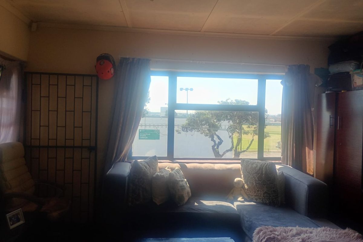 A living room featuring a large window with natural light and a security gate, showing signs of wear on the ceiling and walls.