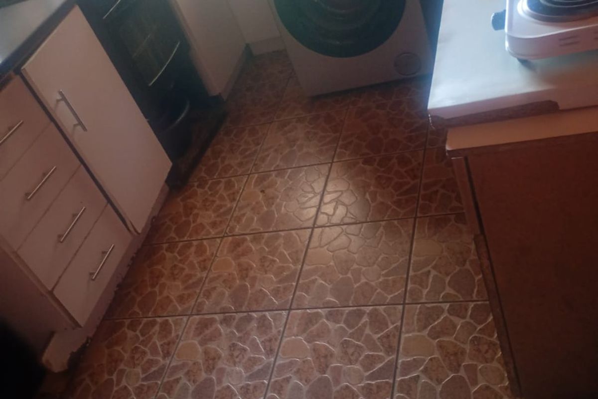A compact kitchen featuring built-in cabinetry, tiled flooring, and an integrated oven, offering a functional layout in need of cosmetic updates.