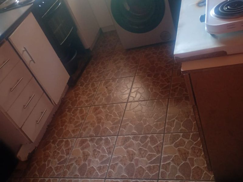 A compact kitchen featuring built-in cabinetry, tiled flooring, and an integrated oven, offering a functional layout in need of cosmetic updates.