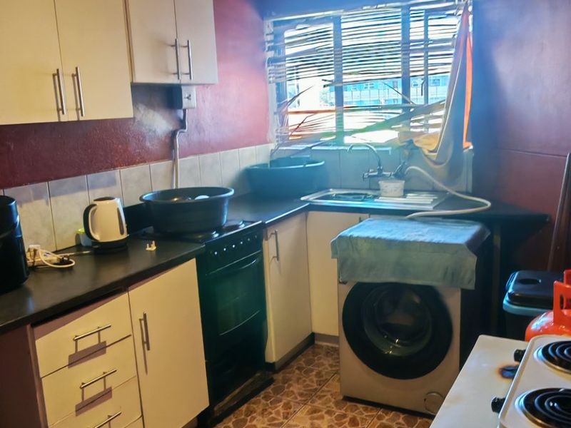 A compact kitchen featuring built-in cabinetry, tiled flooring, and a stainless steel sink, currently showing significant signs of ceiling water damage and wear.