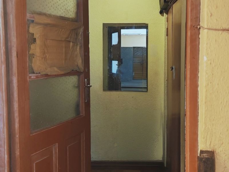 An entry hallway featuring original parquet flooring, a timber door with glass panels, and a built-in cupboard, requiring cosmetic updates and repairs.