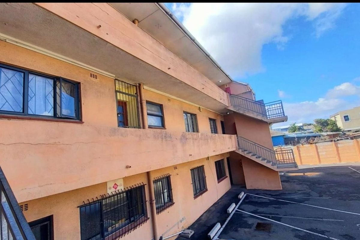 Rear exterior view of an apartment building featuring an external staircase, balcony access, and a paved parking area with security bars on windows.