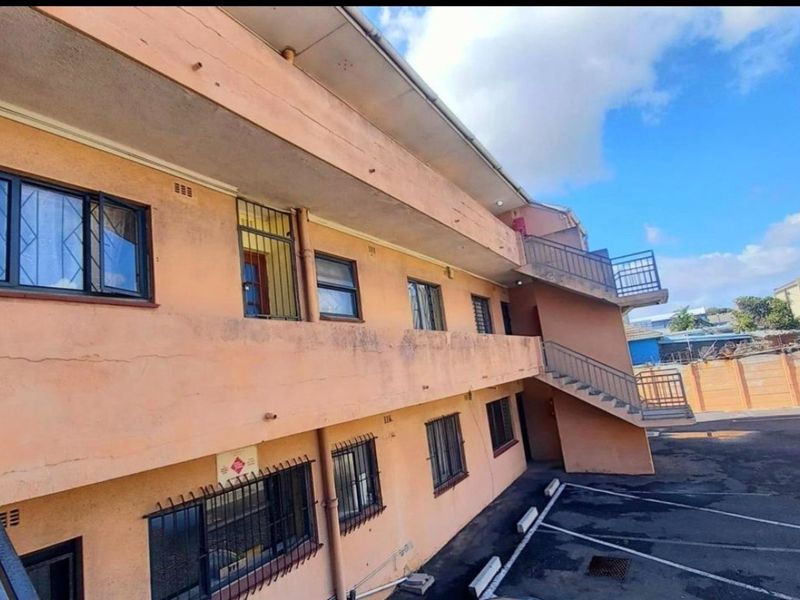Rear exterior view of an apartment building featuring an external staircase, balcony access, and a paved parking area with security bars on windows.