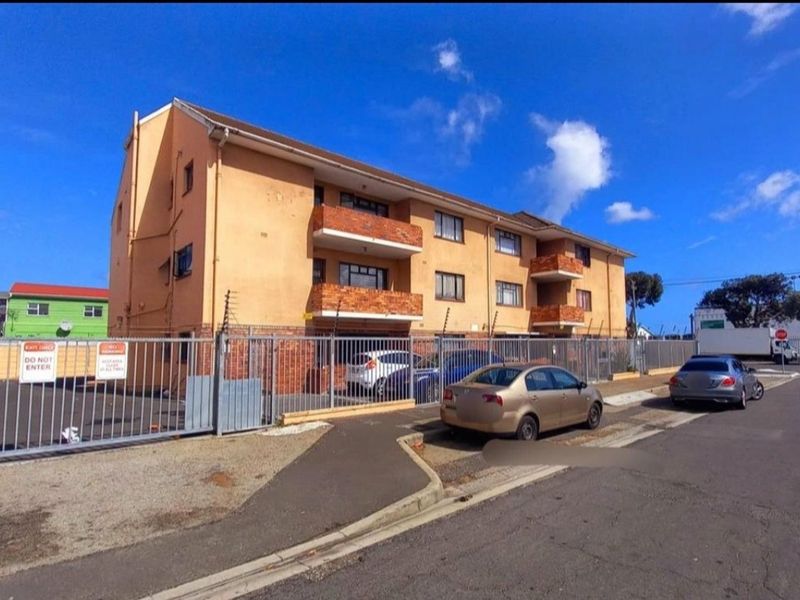 Street-level view of a multi-story apartment building featuring brick balconies, secure perimeter fencing, and gated access.