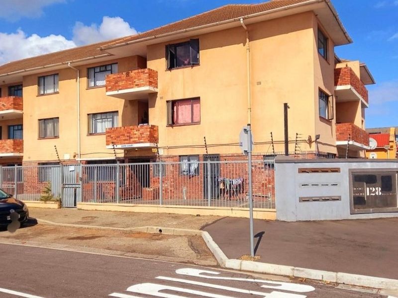 Exterior view of a multi-story apartment building featuring brick balconies, secure perimeter fencing with electric security wires, and a dedicated post box area.