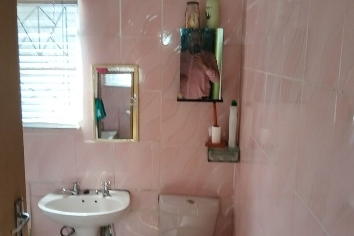 A dated bathroom featuring pink wall tiles, a pedestal basin, and a standard toilet, requiring modernization and cosmetic updates.