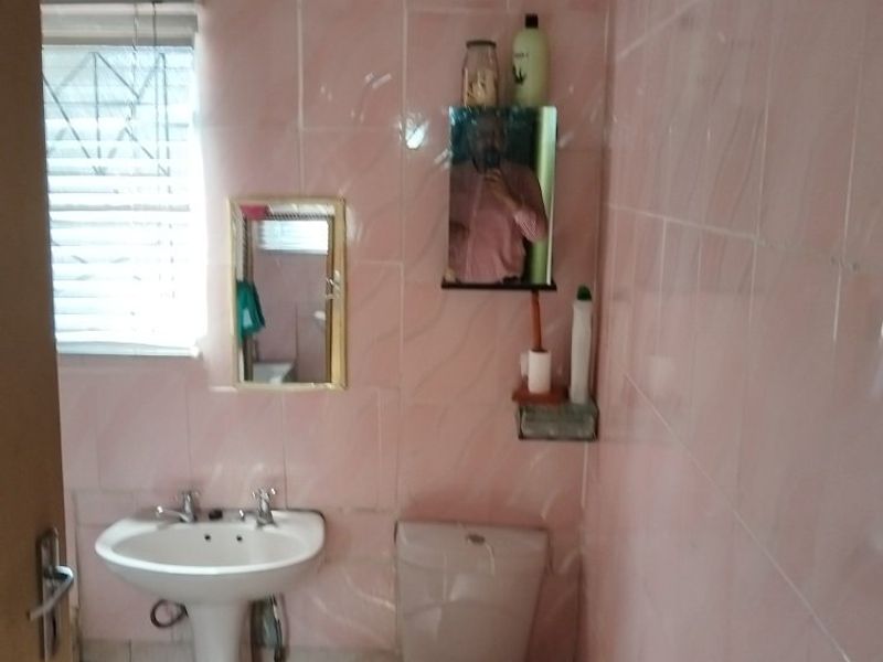 A dated bathroom featuring pink wall tiles, a pedestal basin, and a standard toilet, requiring modernization and cosmetic updates.