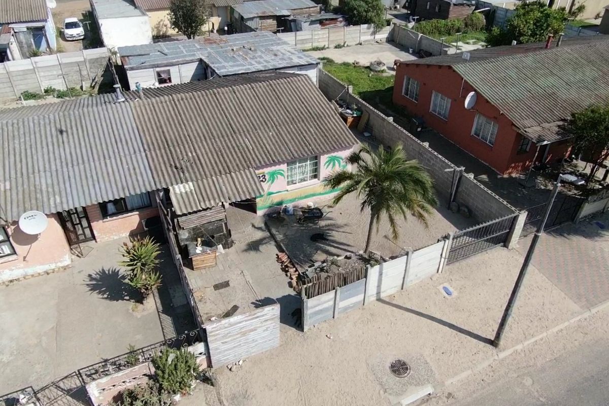 Aerial view of a residential property featuring a corrugated metal roof, enclosed yard with precast concrete boundary walls, and a gated entrance.