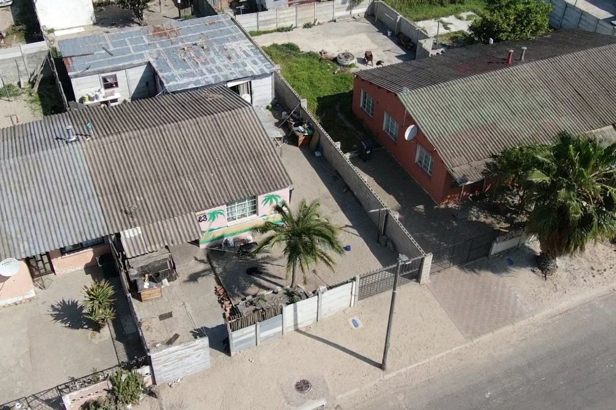 Aerial view of the property showing the residential building, corrugated roofing, boundary walls, and driveway access from the street.