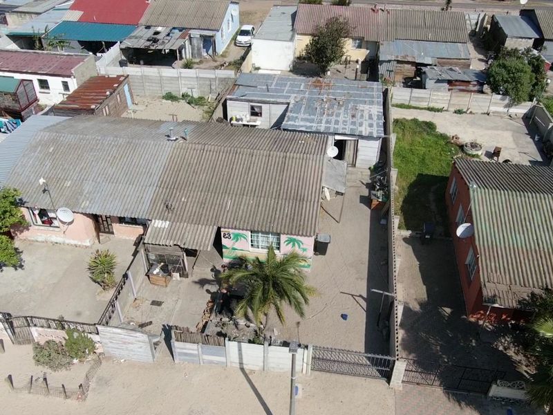 Aerial view of a residential property featuring a corrugated metal roof, enclosed yard with precast concrete boundary walls, and a metal entrance gate.
