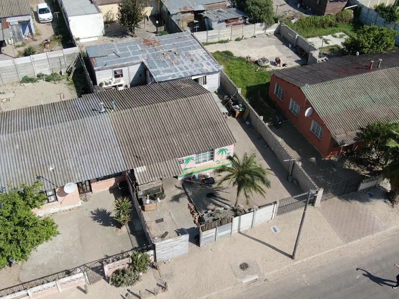 Aerial view of a residential property featuring a corrugated metal roof, enclosed yard with precast concrete boundary walls, and a concrete driveway.