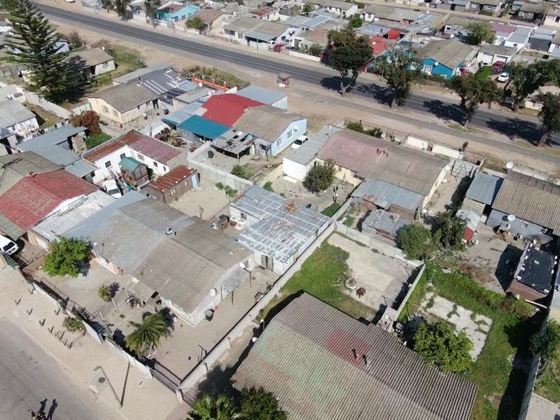 An aerial view of a residential neighborhood showing multiple properties with corrugated metal roofs, boundary walls, and surrounding street infrastructure.