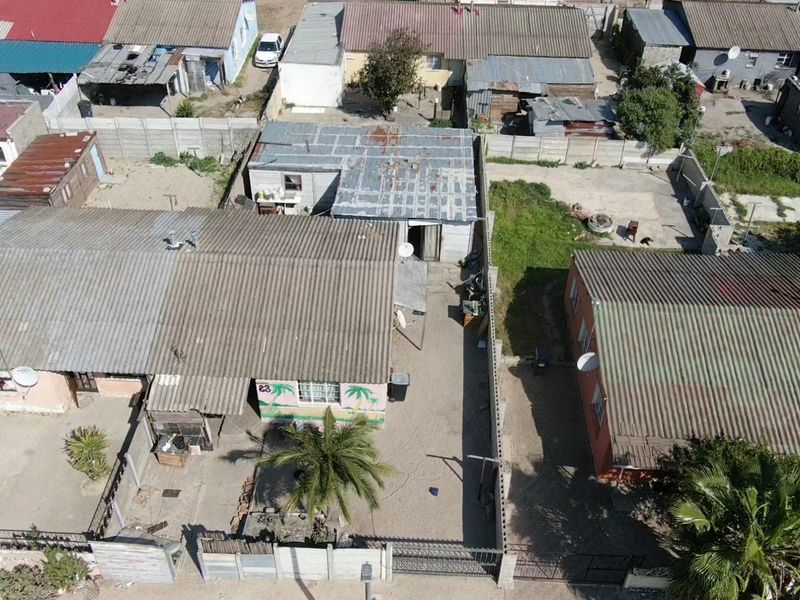 Aerial view of a residential property featuring a main dwelling with corrugated metal roofing, a fenced yard, and surrounding neighborhood context.