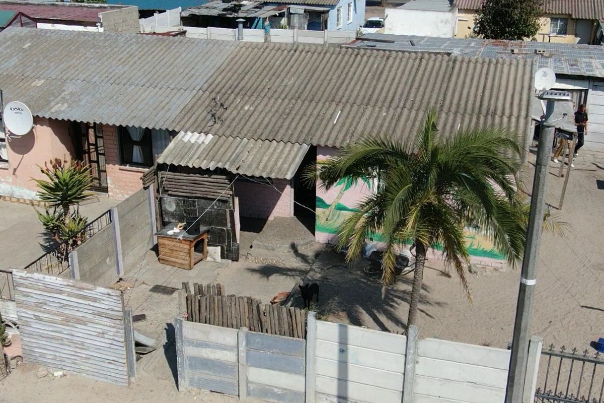 Aerial view of a residential property featuring a corrugated roof, precast concrete boundary walls, and an unpaved yard area.