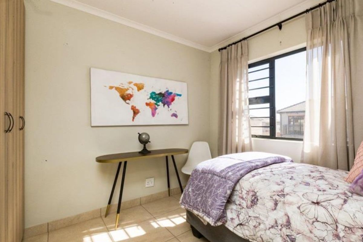 A functional bedroom featuring tiled flooring, a built-in wardrobe, and natural light through an aluminium-framed window.
