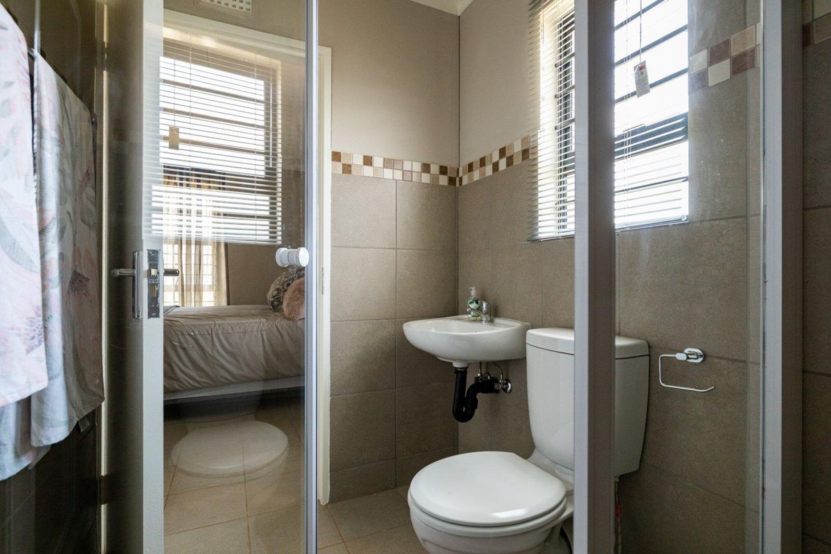 A compact bathroom featuring tiled walls, a wall-mounted basin, a toilet, and a glass shower enclosure, with natural light from a window.