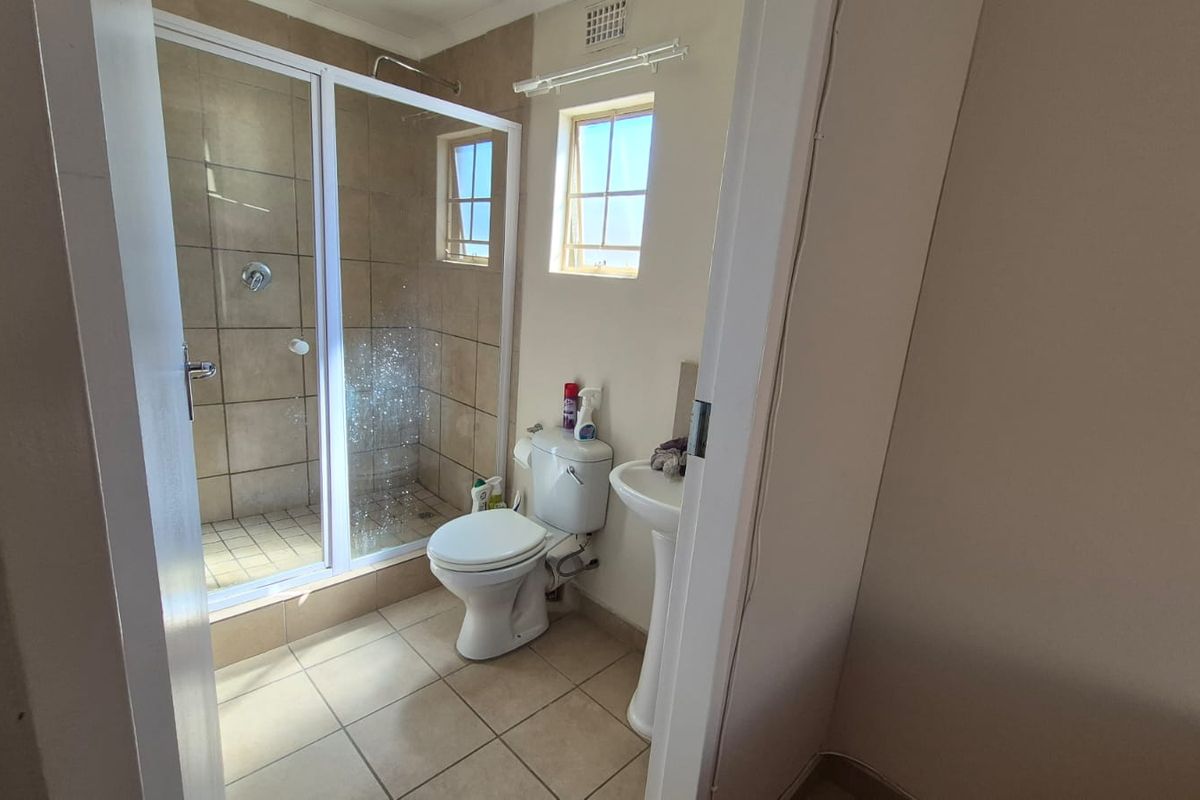 A functional bathroom featuring a tiled shower enclosure, pedestal basin, and toilet with neutral wall finishes and natural light from a casement window.