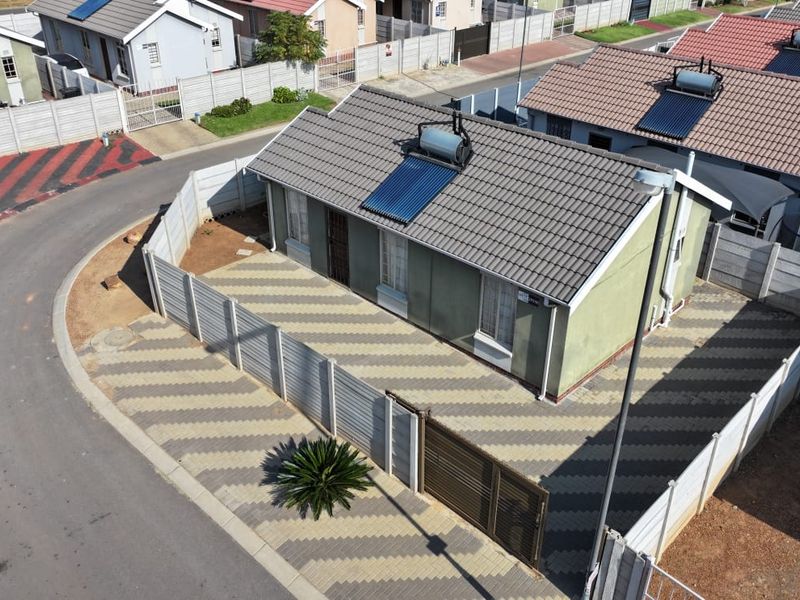 Aerial view of a residential property featuring a tiled roof with a solar water heater, paved driveway, and secure perimeter walling.